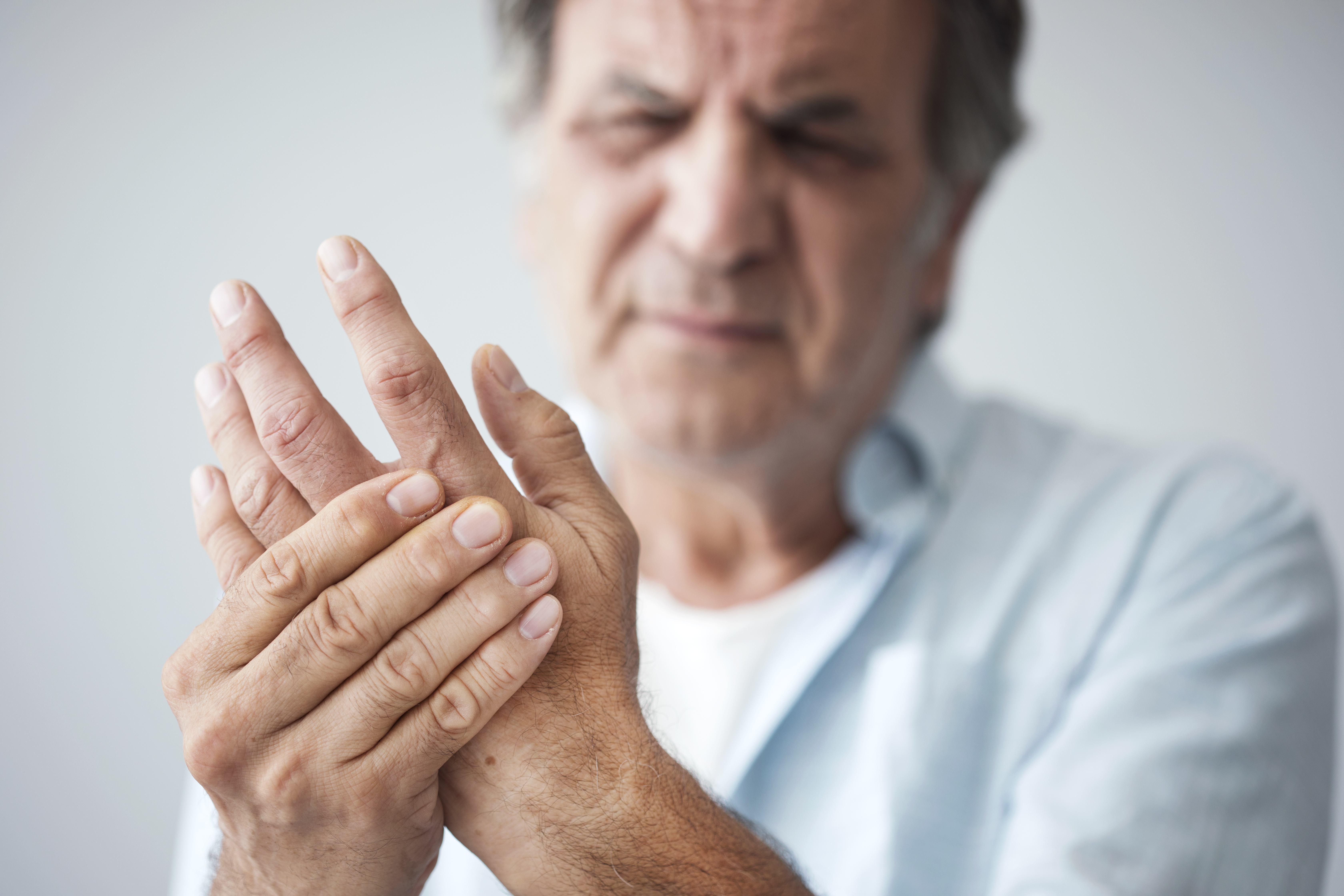 An older man cringing and holding his hand in pain from arthritis