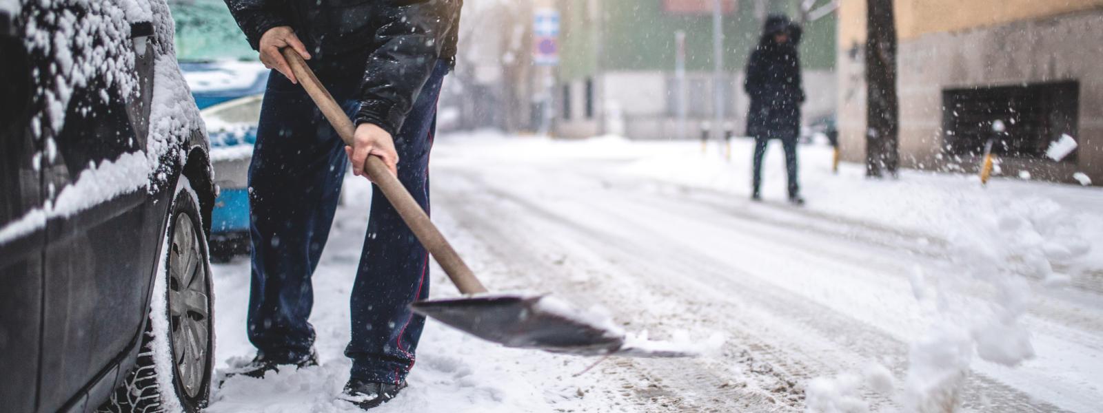 Man shoveling snow in street around cars.