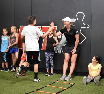 Golf pro Amy Anderson gives high five to kid at Inspira Fitness Connection’s Performance Improvement Training program