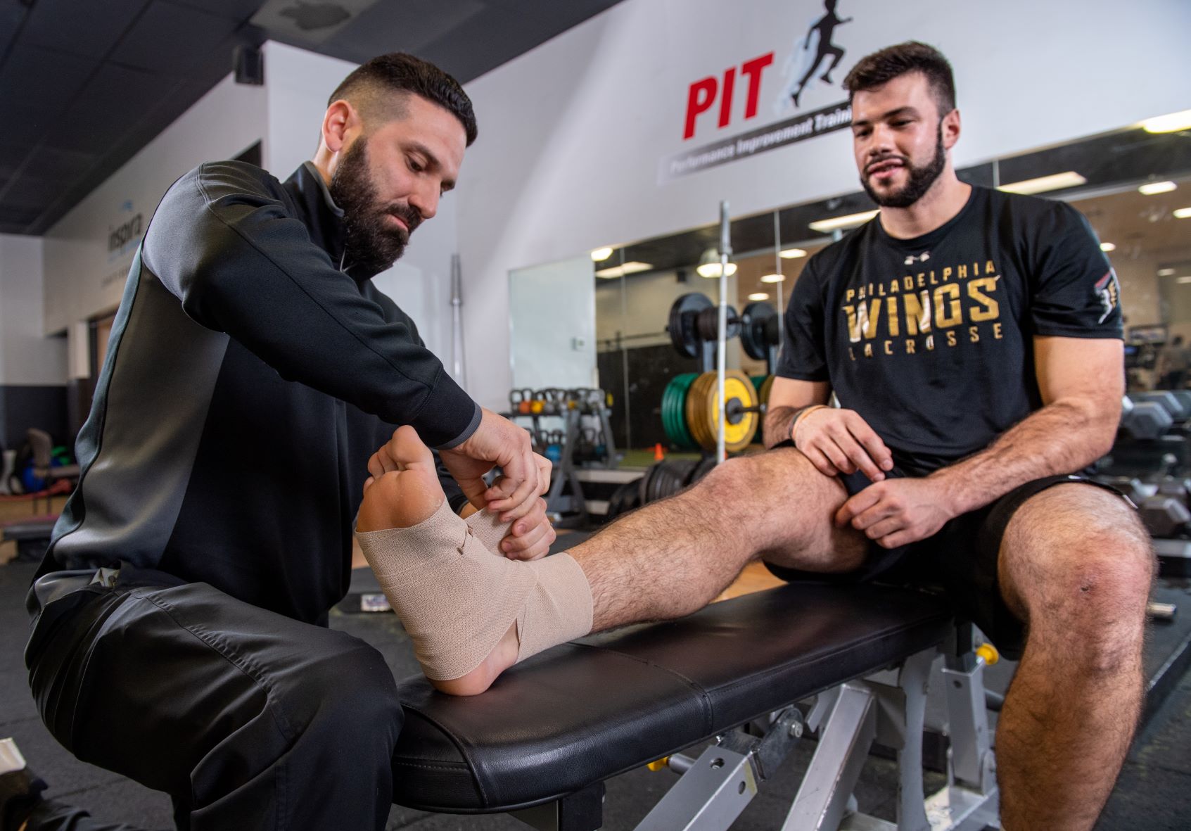 Man wrapping athlete's ankle with an ace bandage in a gym