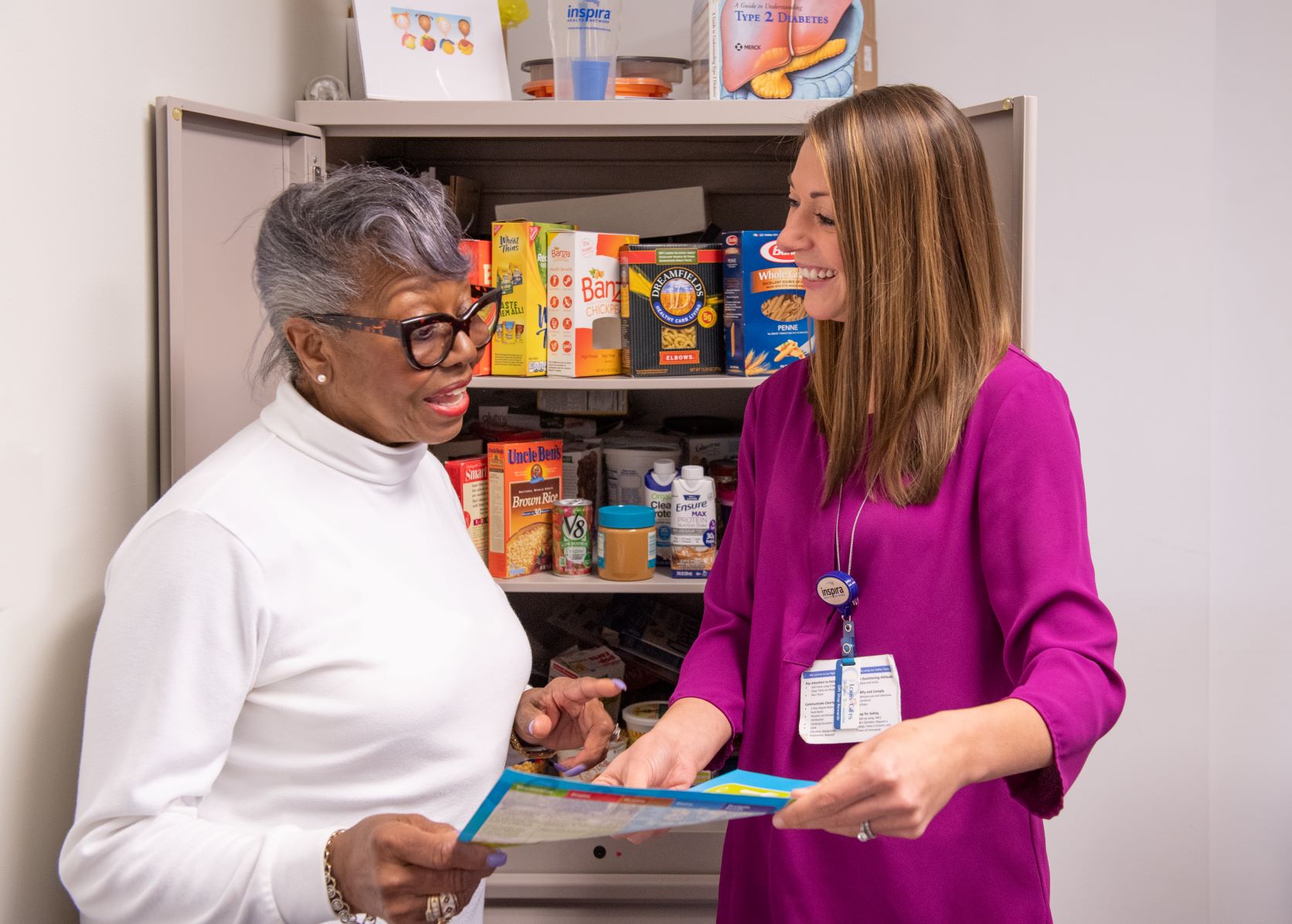 Nutrition counselor reviewing paper with patient in front of open pantry with healthy foods