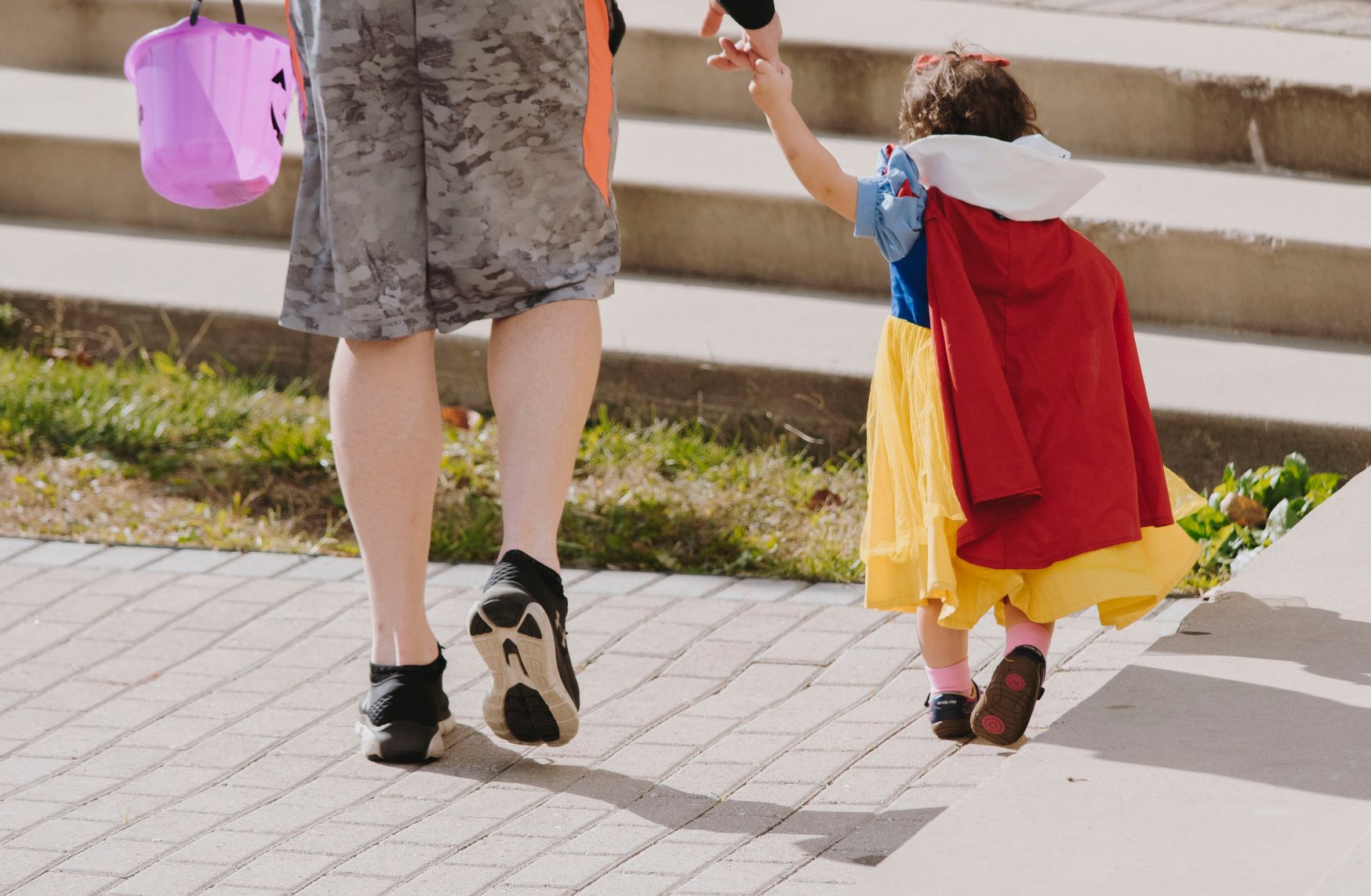 Man holding halloween pumpkin bucket holding a young girl dressed as Snow White