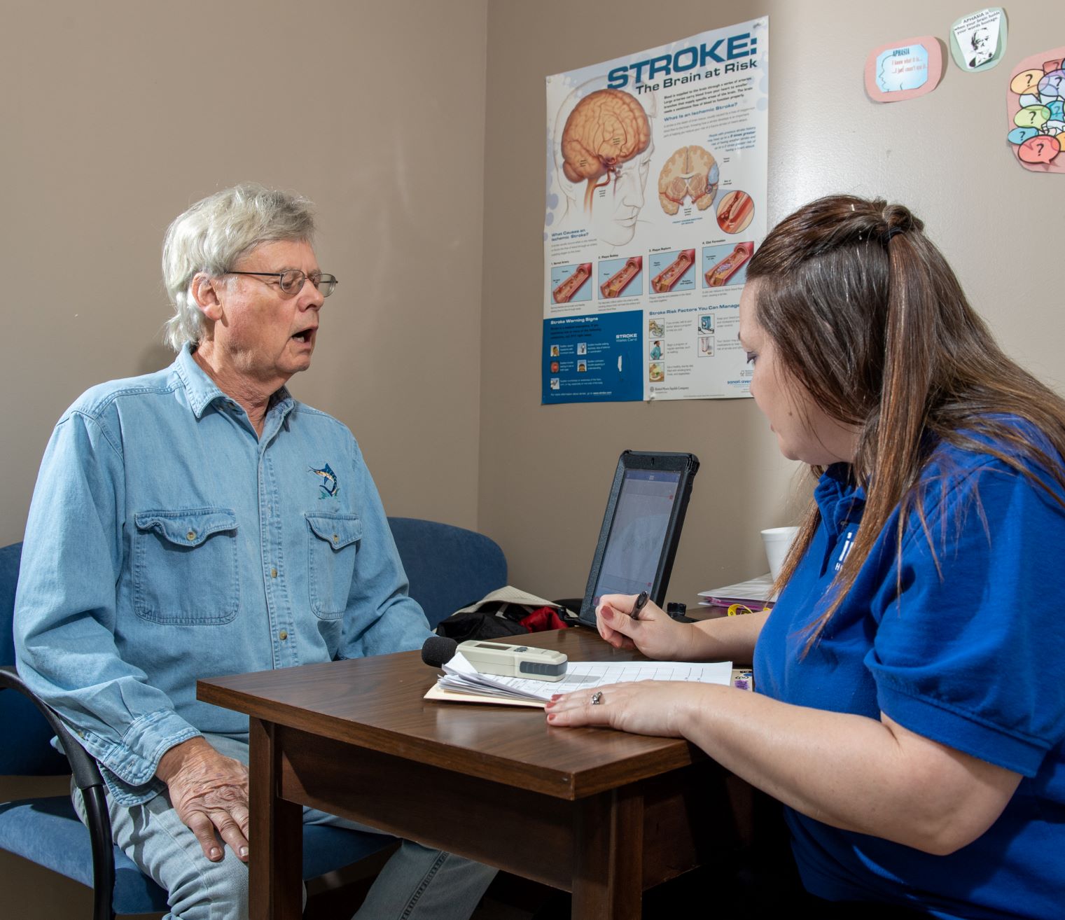 An older person doing speech exercises with a speech language pathologist at a table