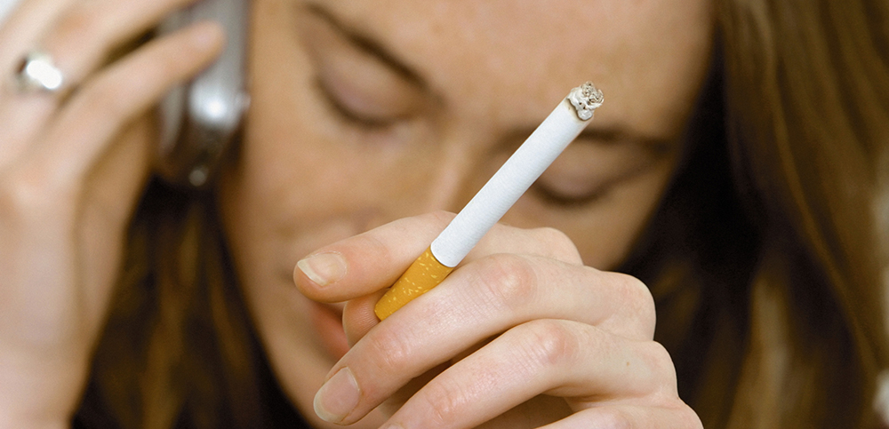 A woman looking downwards, smoking a cigarette