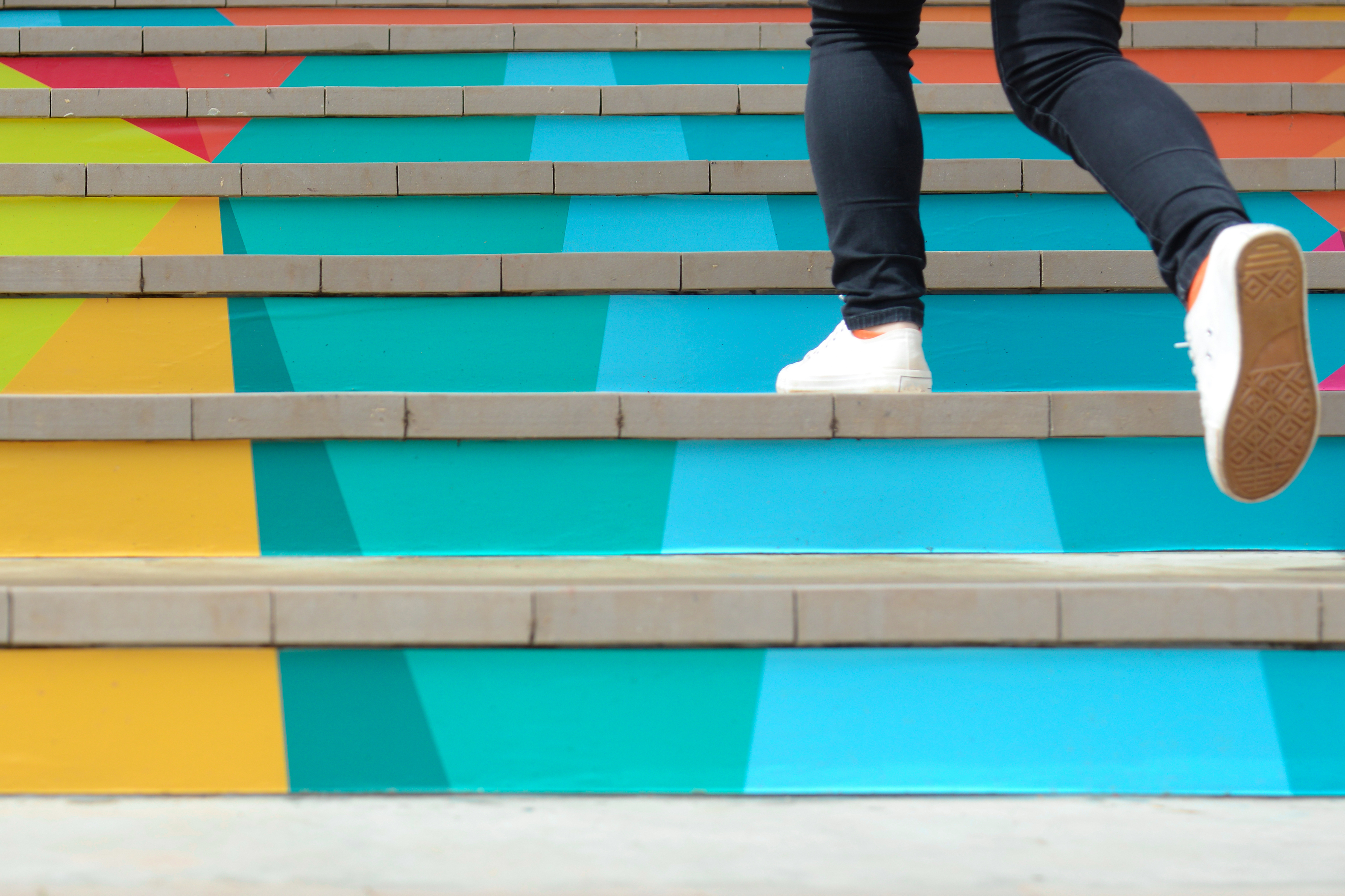 Someone wearing white sneakers walking up a colorful staircase
