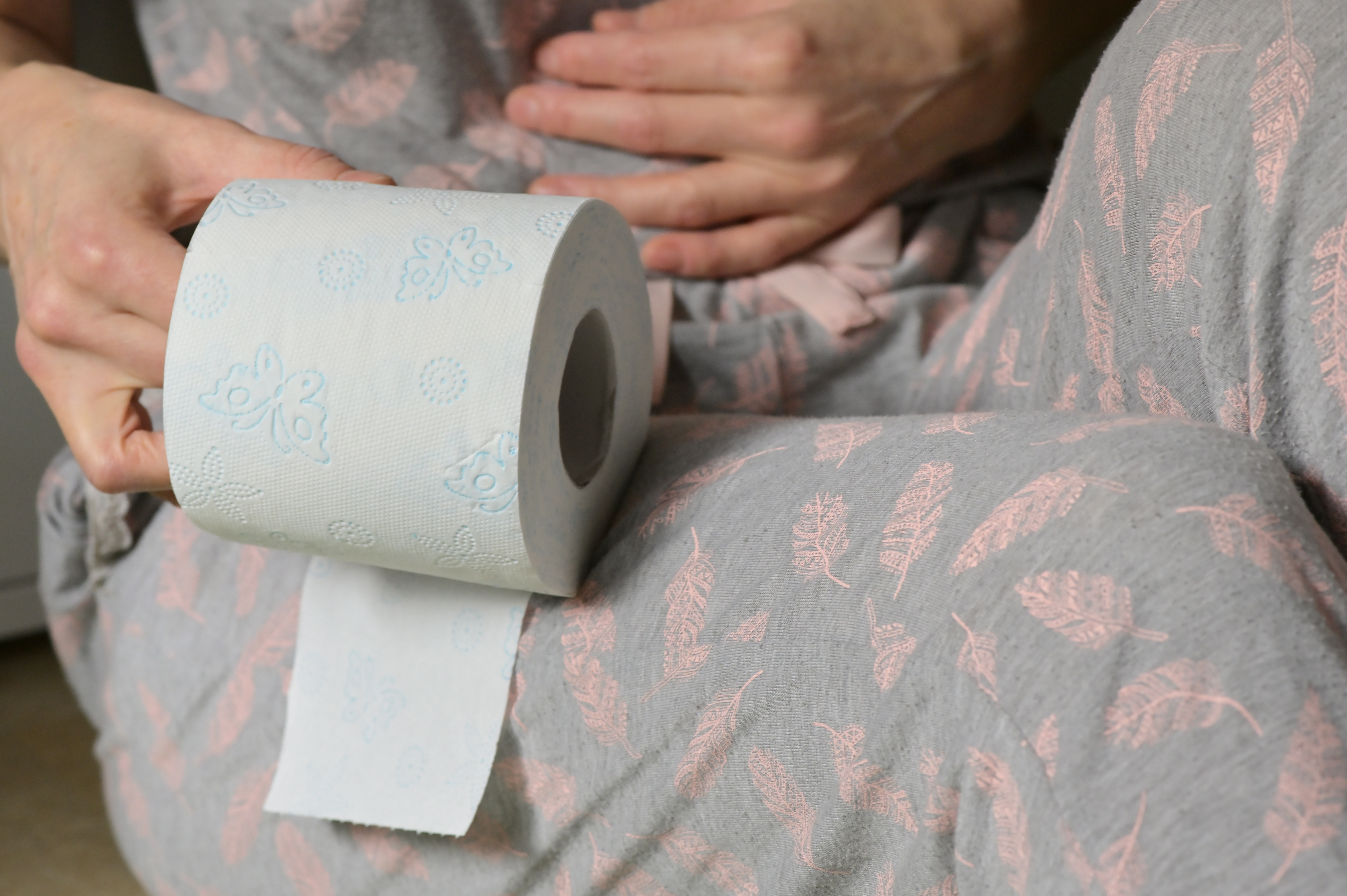 A person holding their stomach and holding a roll of toilet paper