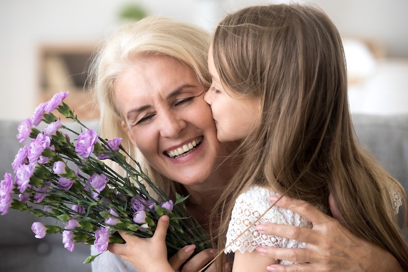 olderwoman being given flowers and a kiss on the cheek by young girl