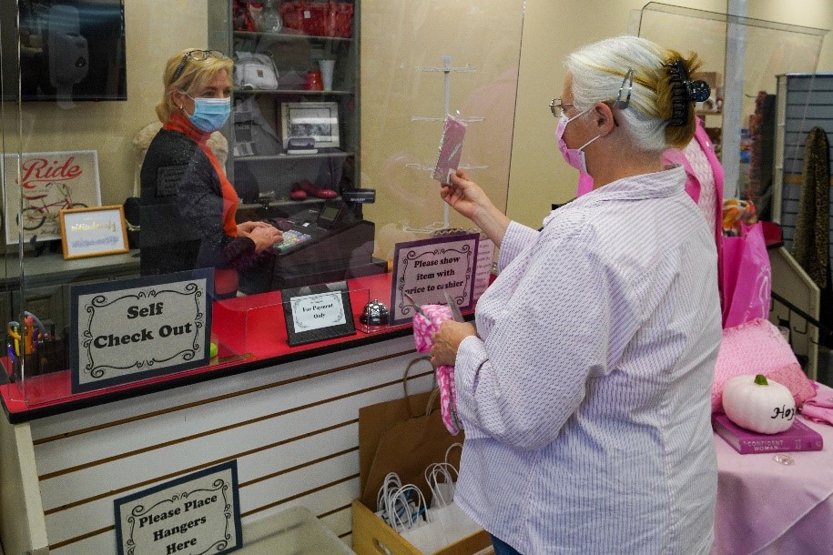 Store Manager Holly Kennedy, at the register, and Linda Burgess, salesperson, show how a plastic shield protects the staff and the shopper during the self-checkout process at Twice Loved Treasures Thrift Shop.