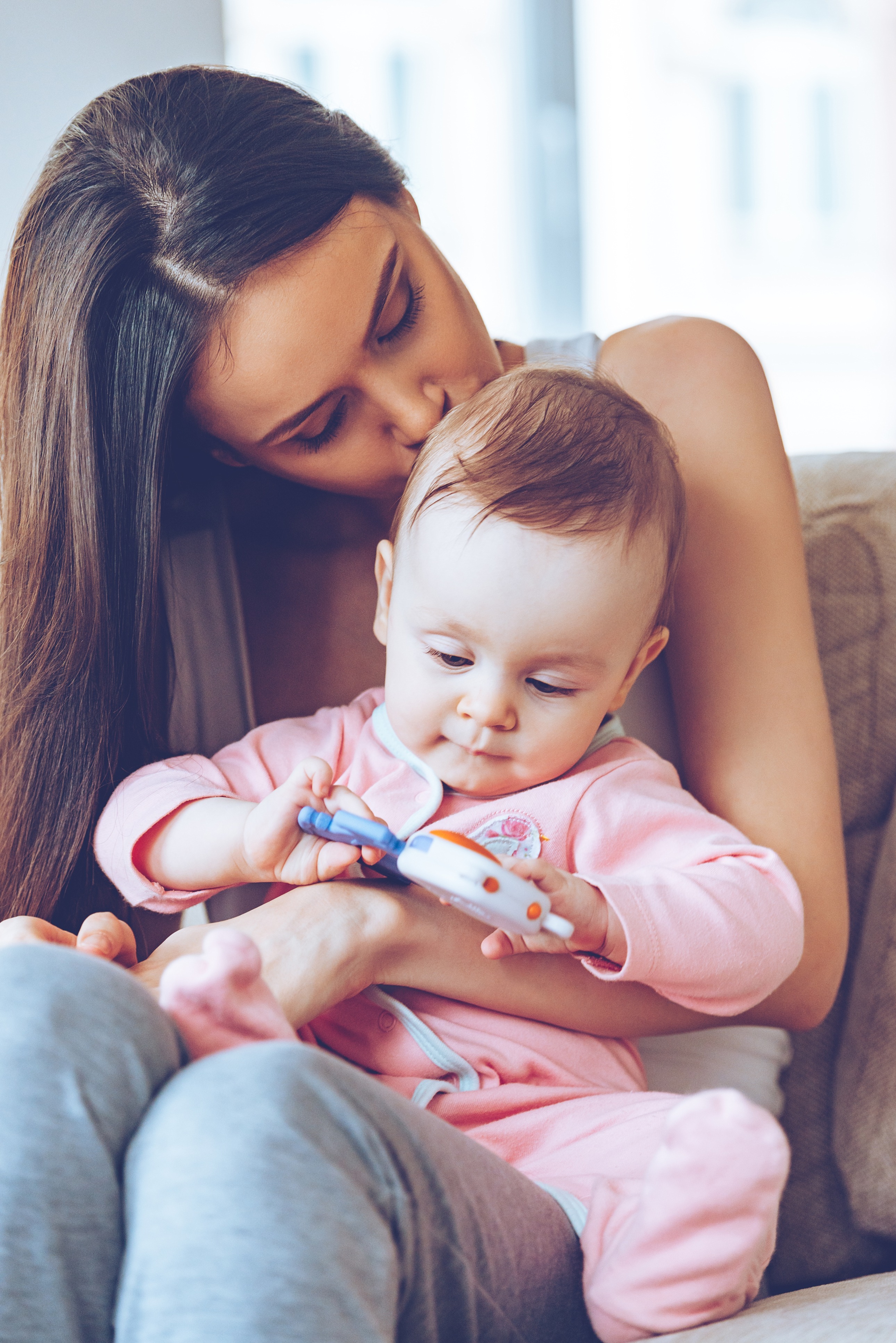 woman kissing a baby's head on her lap who is playing with a rattler