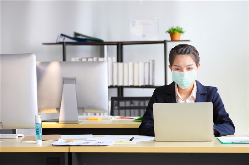Female employee wearing medical face mask while working alone because of social distancing policy in the business office during coronavirus or covid-19 outbreak pandemic situation