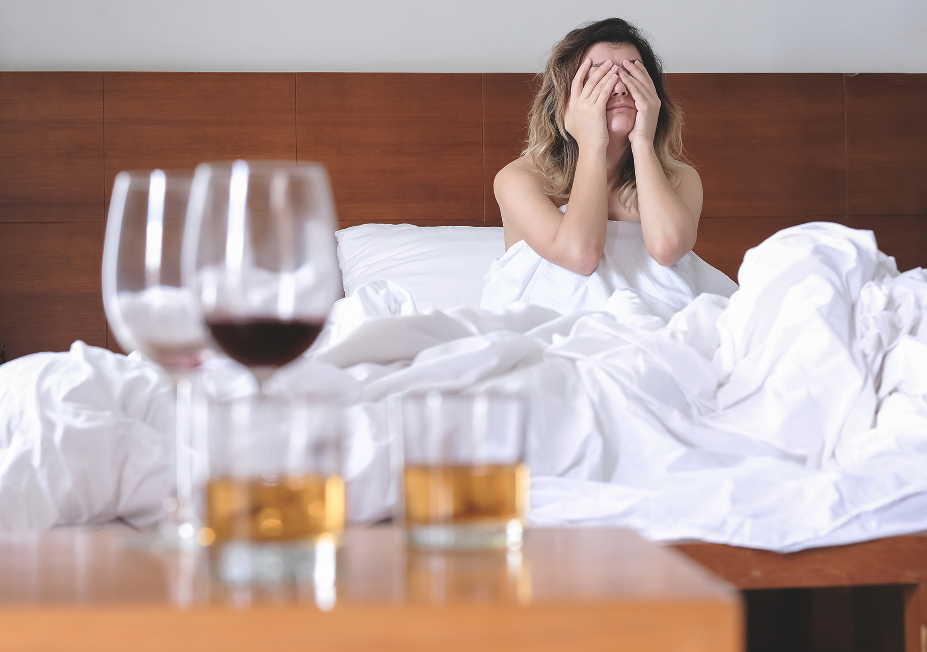 Exhausted woman in bed with wine and tumblers on a nearby table