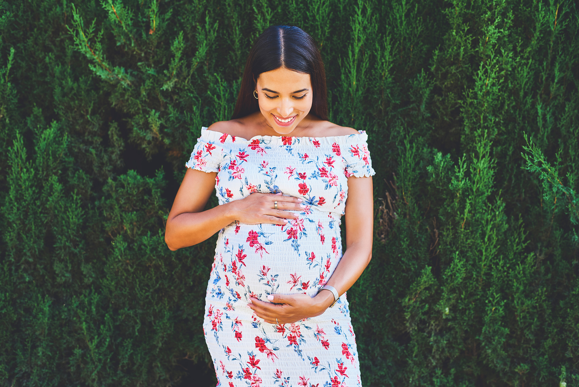 Cropped shot of a young pregnant woman posing outside against bushes in a park