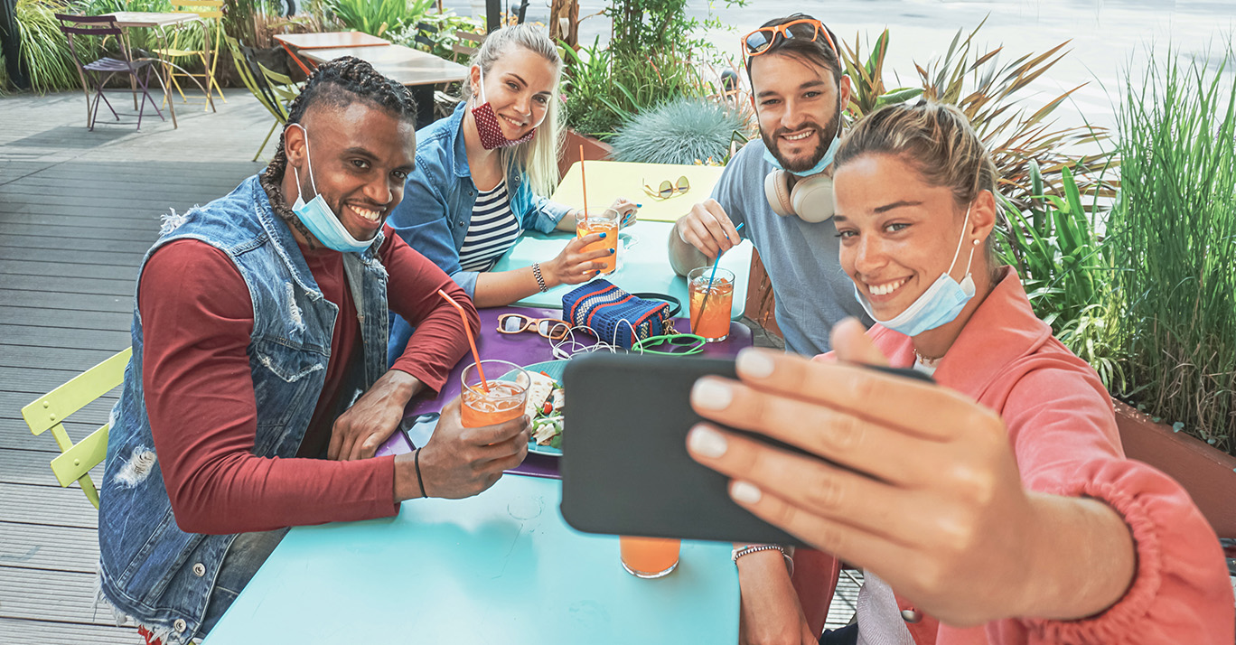Friends takeing selfie in a bar restaurant with face mask on in coronavirus time - Young people having fun with drinks and snacks outside with new rules after virus break stock photo