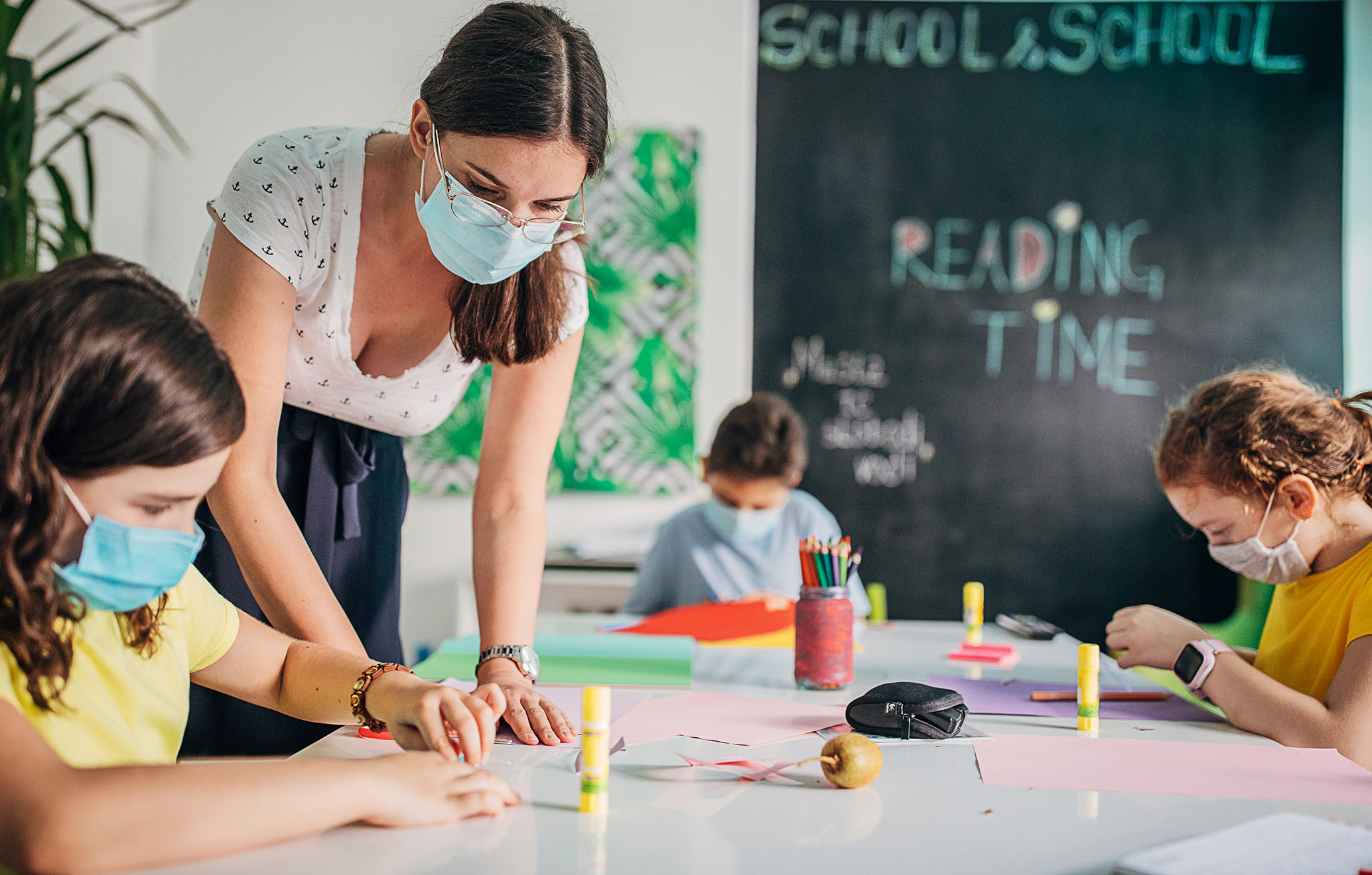 Children and female teacher together on class in private school classroom, they are wearing surgical masks do to coronavirus spreading.