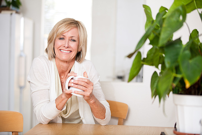 cheerful middle aged woman sitting at a table drinking from a mug