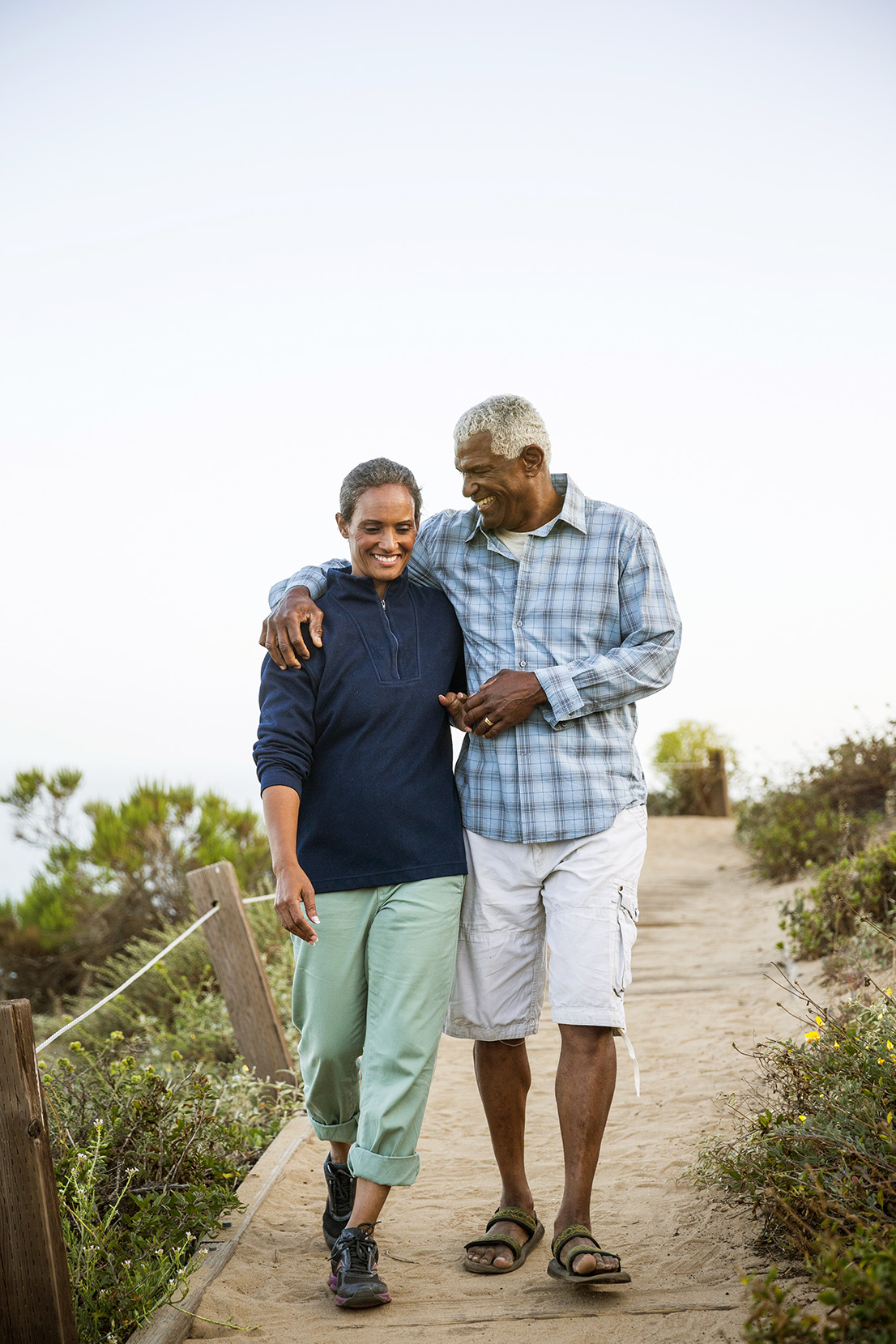 Senior african american couple casually dressed waling together on a boardwalk outdoors near the beach.