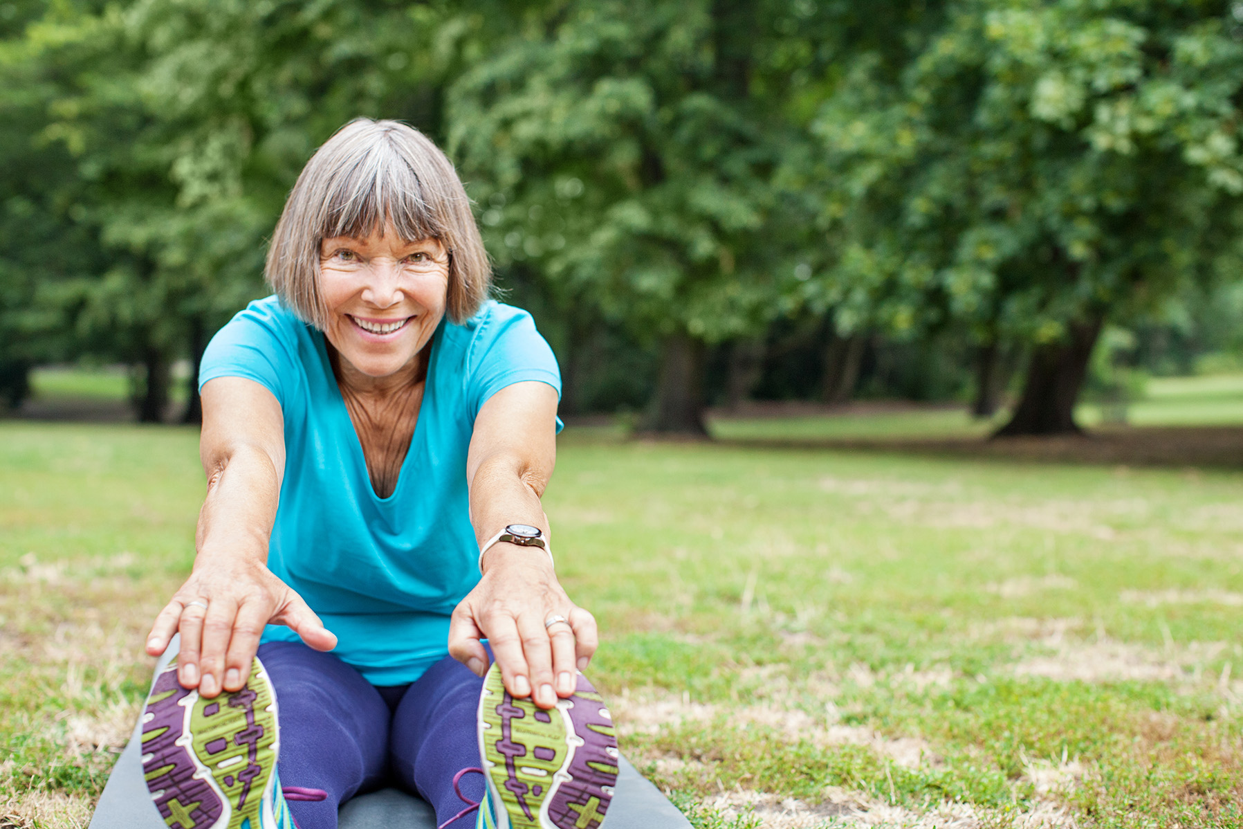 Portrait of fit elderly woman doing stretching exercise on yoga mat in park