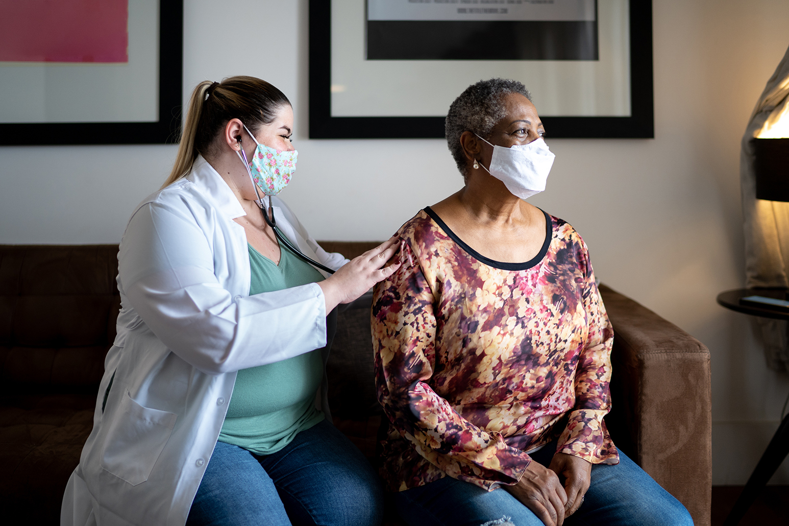 Doctor using stethoscope listening to senior patient breathing at her house - using face mask