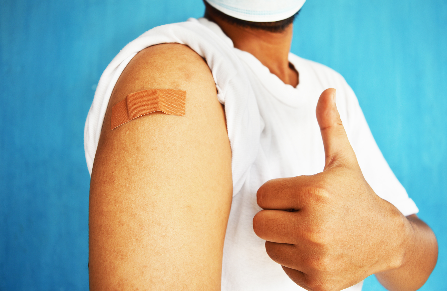 Asian man using adhesive bandage plaster on her arm showing thumb up gesture after injection vaccine.