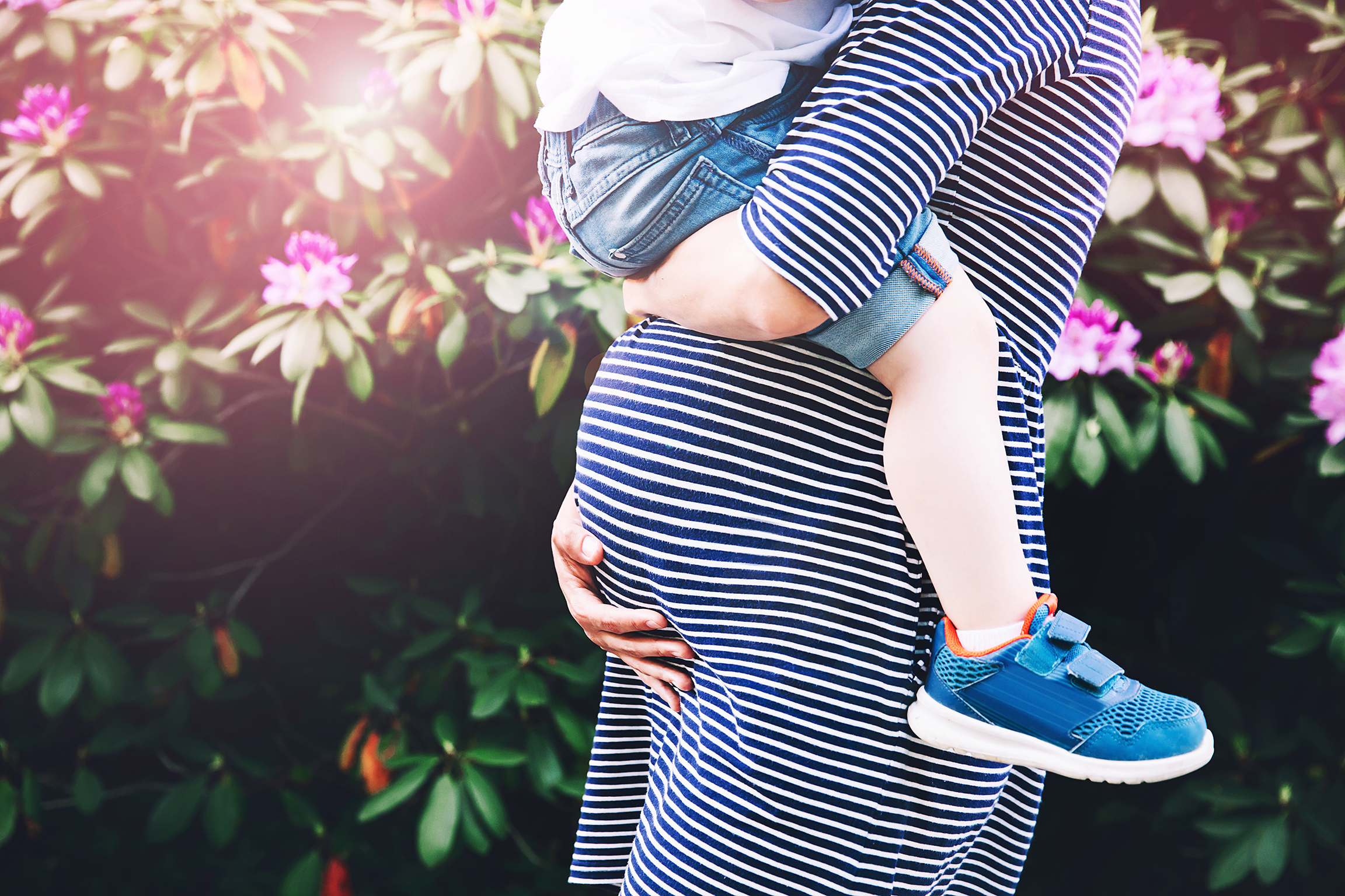 Pregnant woman with child. Mother and son on nature background, close-up. Child boy is sitting on belly of his mother, who pregnant for second time. Pregnancy, new life, family, parenthood concept.