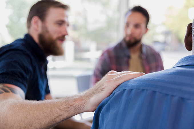 Men in a support group with a hand on each other's shoulder