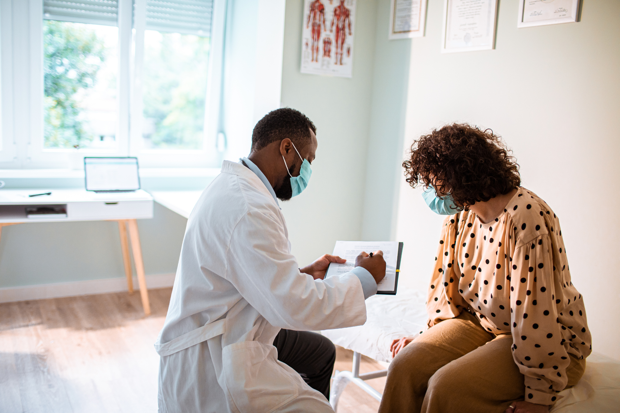 Physician wearing a mask consulting with a masked female patient in a medical office