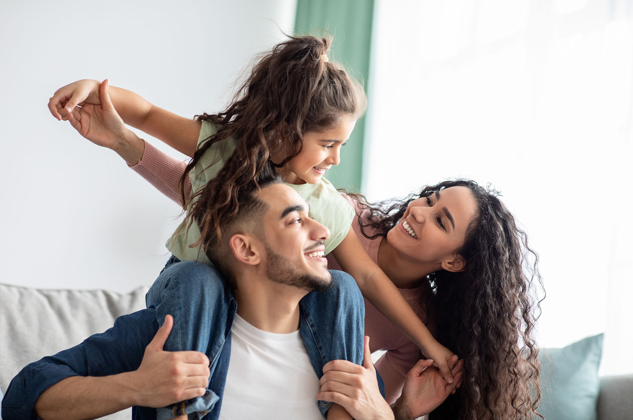 Portraif Of Cheerful Middle Eastern Family Of Three Having Fun Together At Home. Young Arabic Parents Playing With Their Little Daughter In Living Room, Mom, Dad And Child Smiling And Laughing