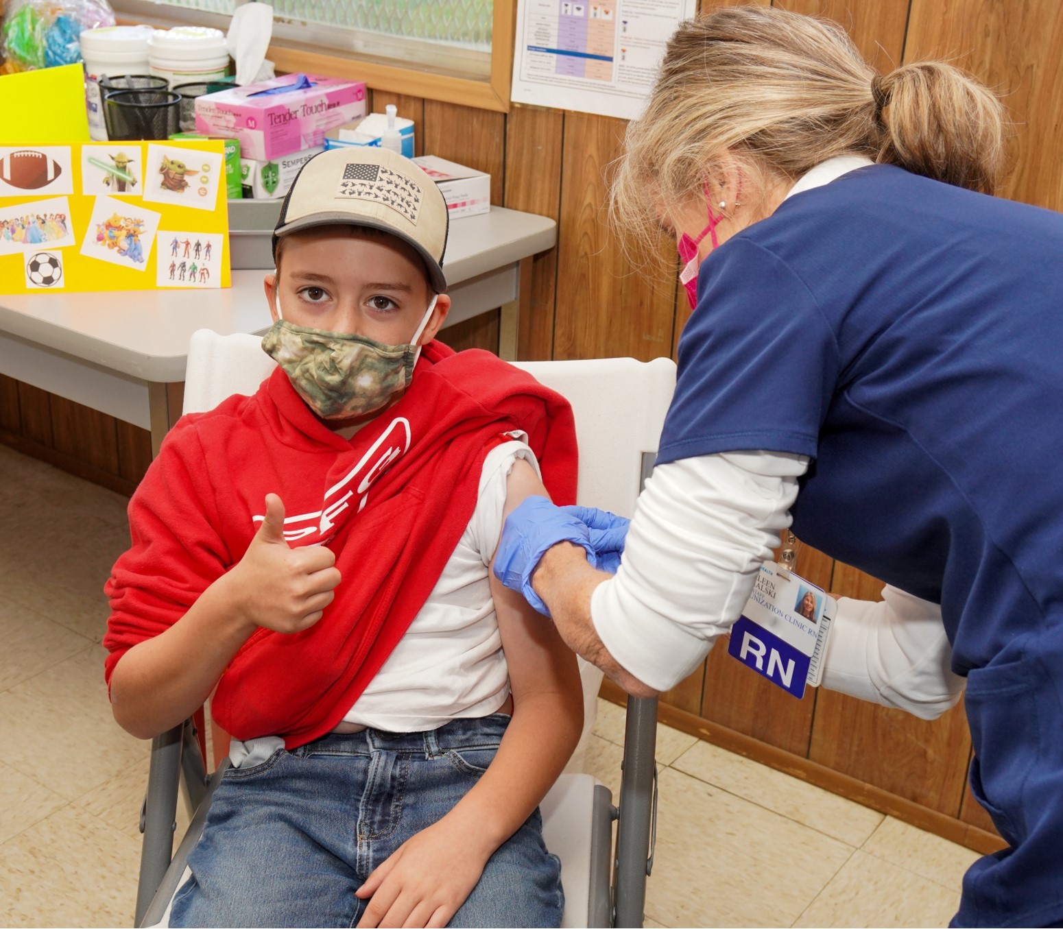 young boy in an hat and face mask receiving the COVID vaccine from an Inspira nurse. 