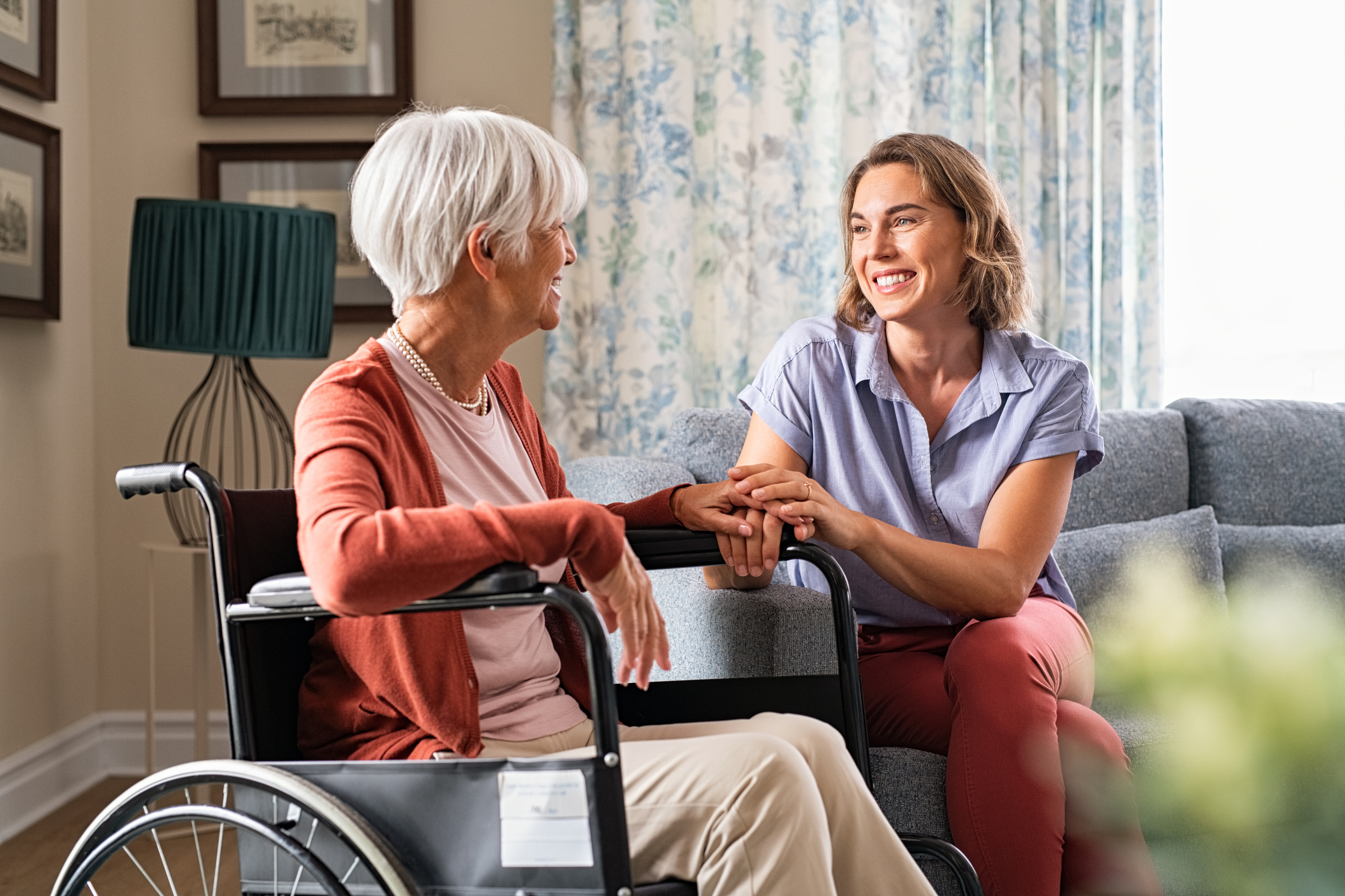 Young woman holding elderly woman's hand while she sits in wheelchair