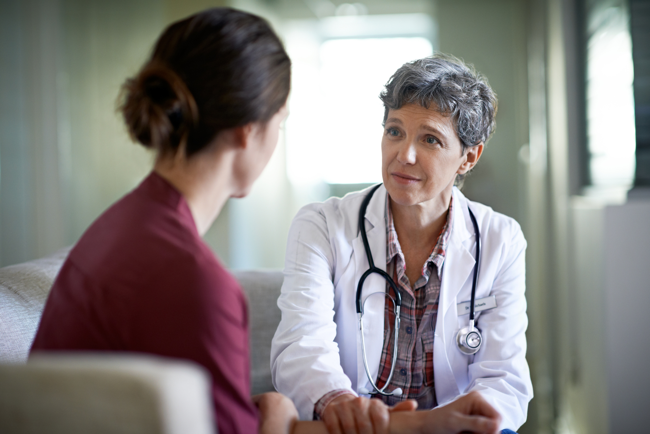 Older female doctor sitting and talking with younger female patient