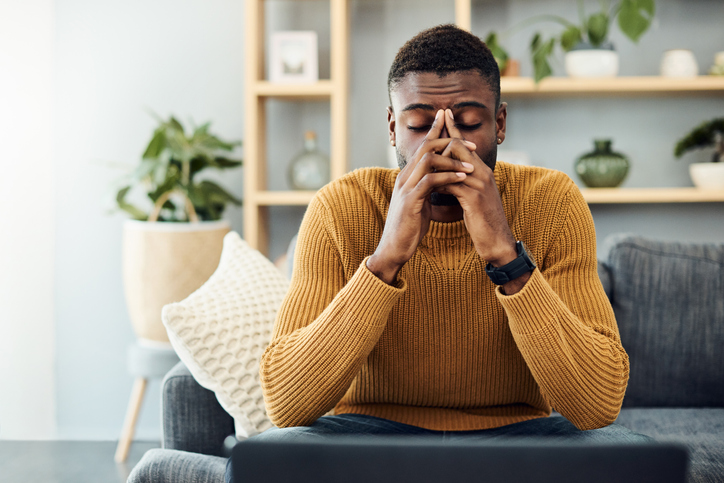 Distressed black man with hands on face on couch