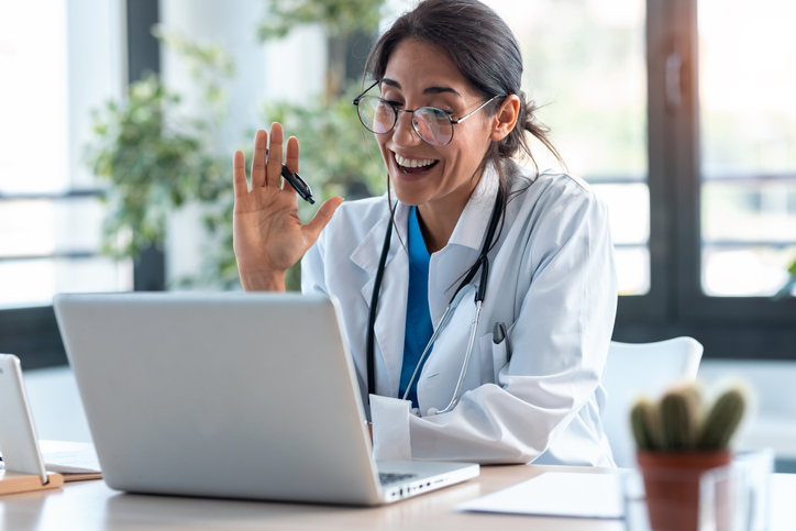 Female teleheath doctor waving to computer