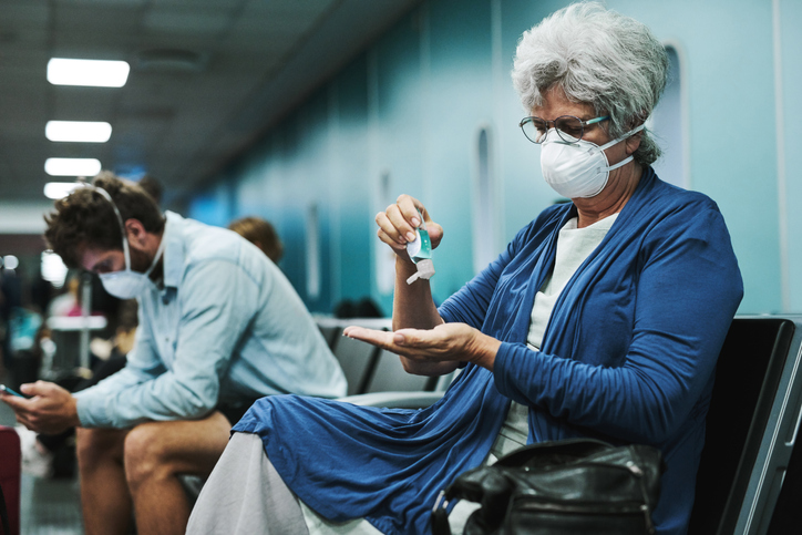 senior woman using hand sanitizer in an airport waiting area