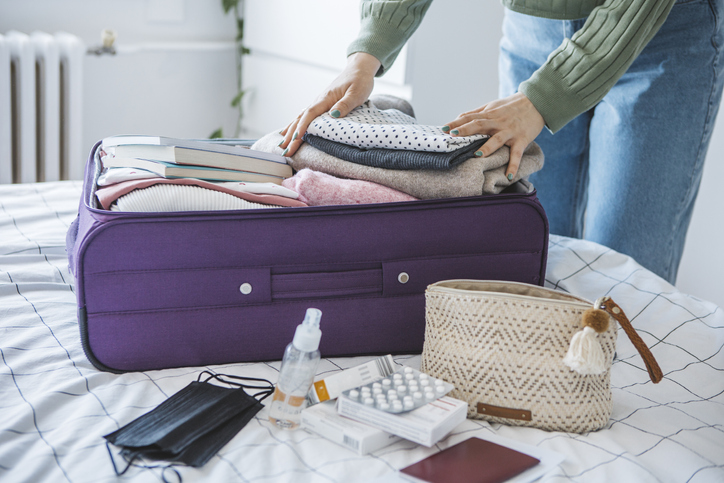 oman preparing travel suitcase on bed at home with medicine and disinfection stuff for travel.