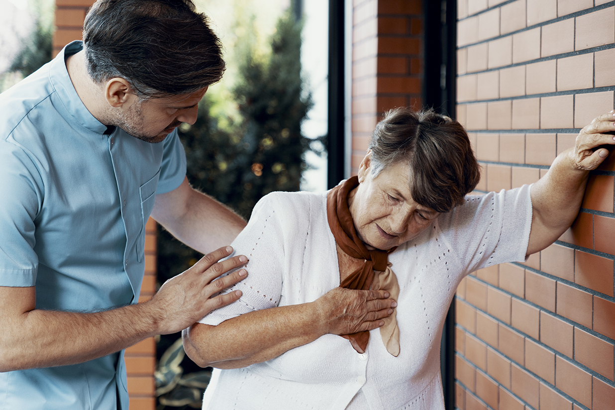 Male nurse helping sick elderly woman with chest pain