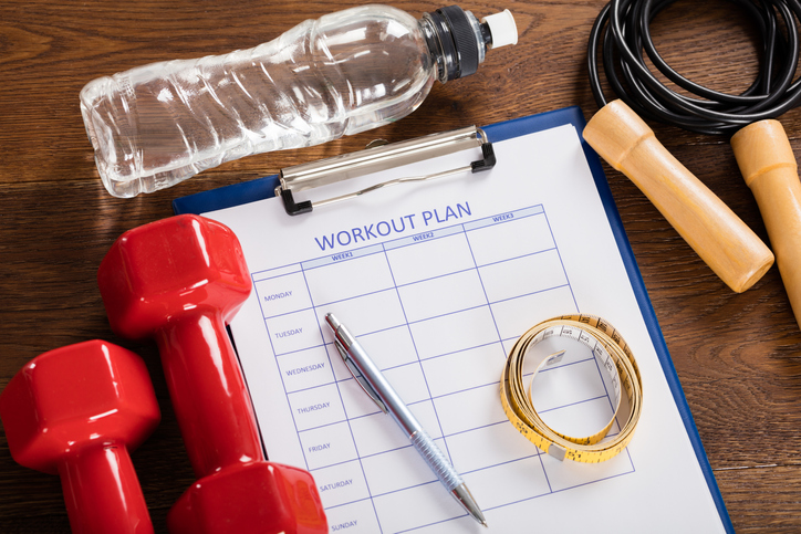 High Angle View Of Workout Plan Form With Fitness Equipments At Desk