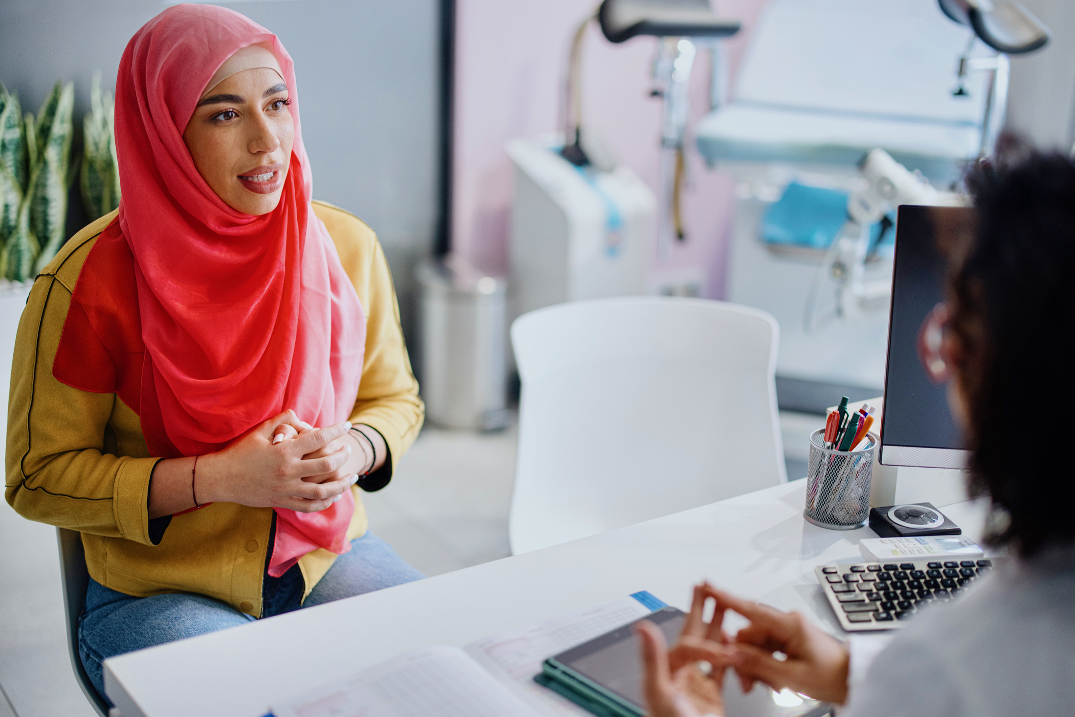 A Muslim woman sits across from her female doctor as she talks with her about cervical cancer