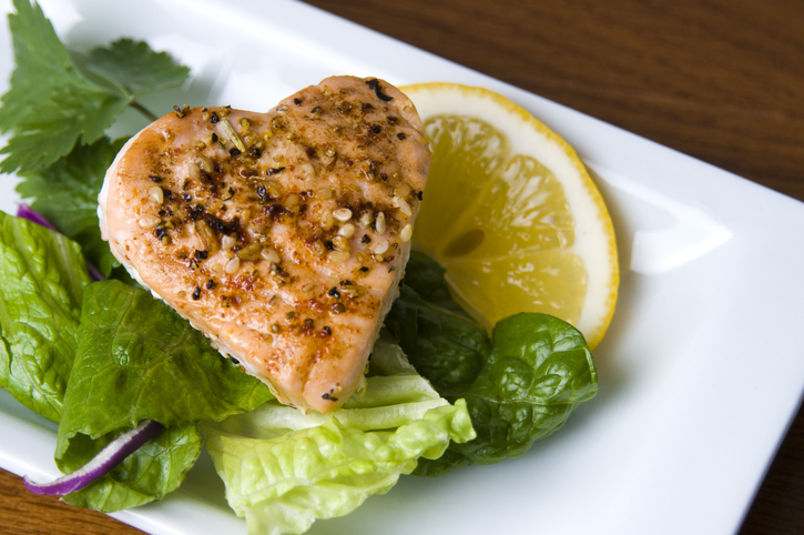 Grilled salmon in a heart shape on salad with slice of lemon