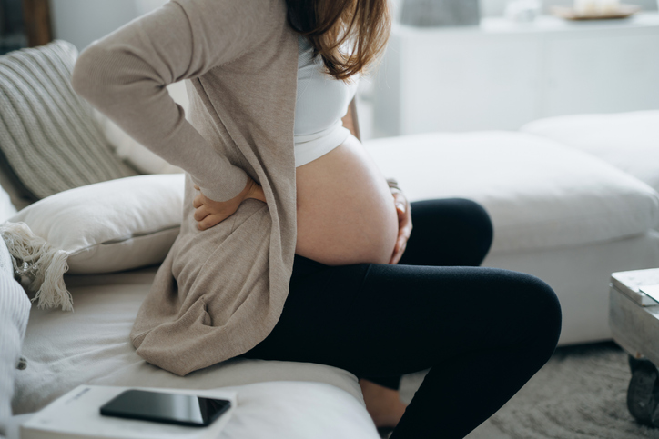 Cropped shot of Asian pregnant woman touching her belly and lower back, suffering from backache