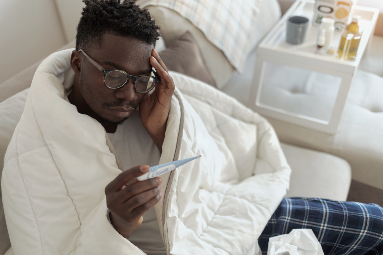 man covered in blanket and checking fever in thermostat 