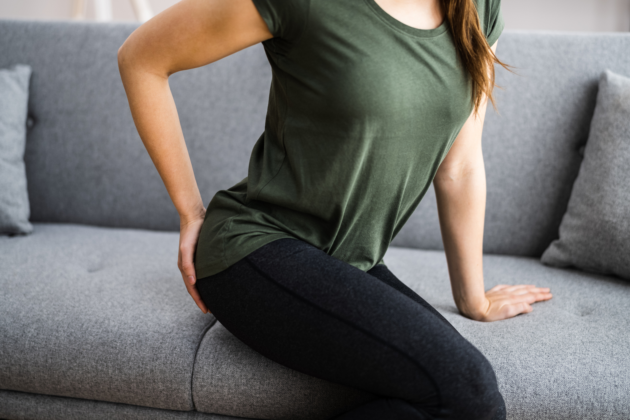 Woman sitting on couch while holding her lower back
