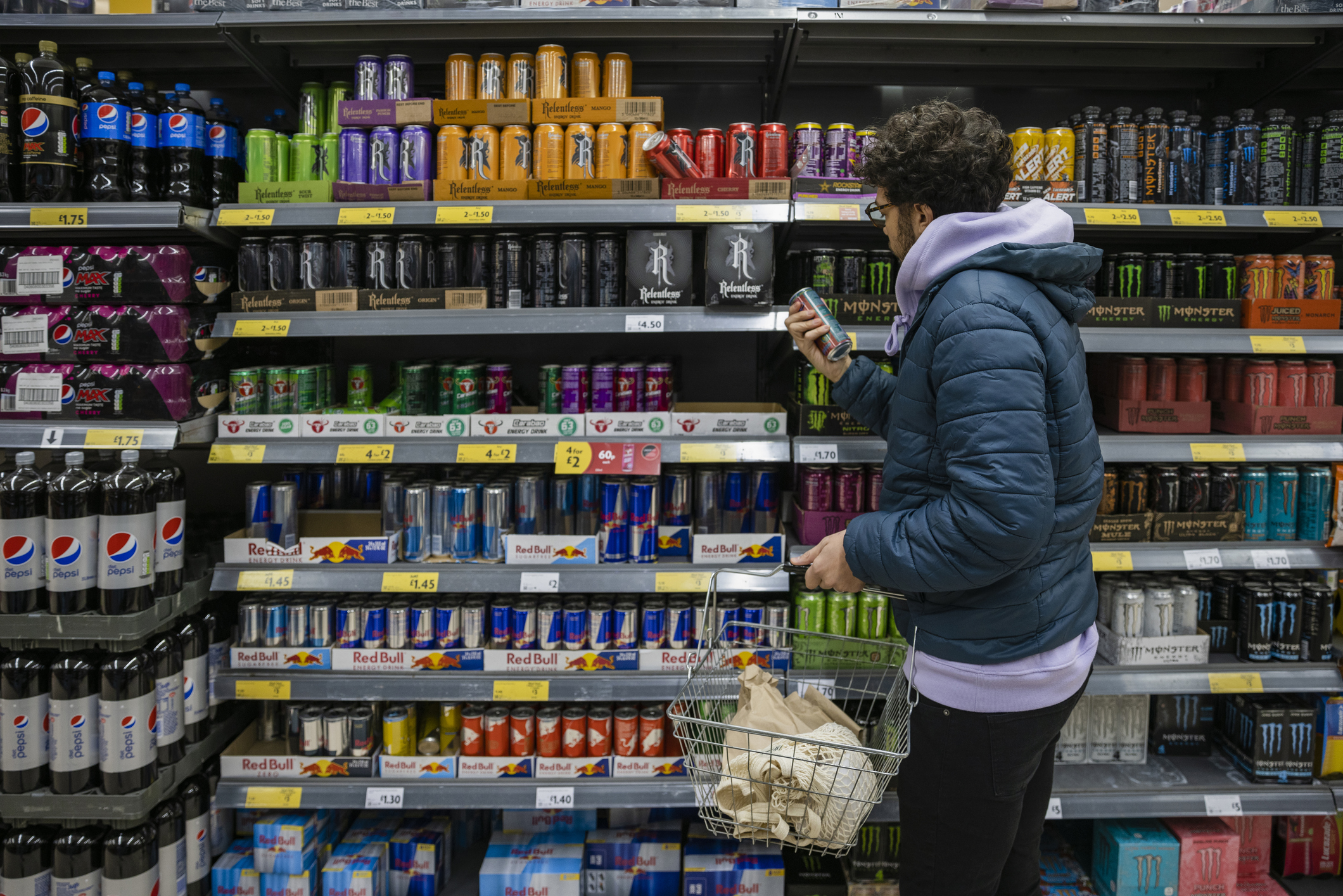 A man reading the nutrition label of an energy drink in a supermarket