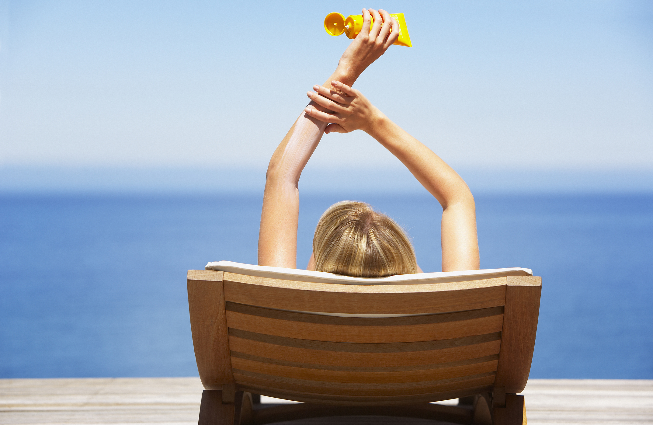 woman applying sunscreen sitting at the beach