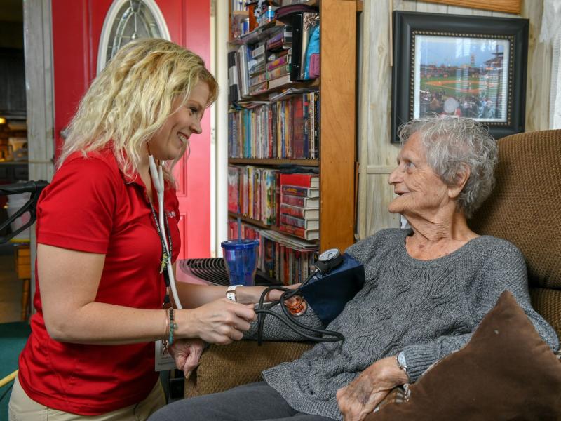 nurse caring for elderly woman at her home by taking her blood pressure