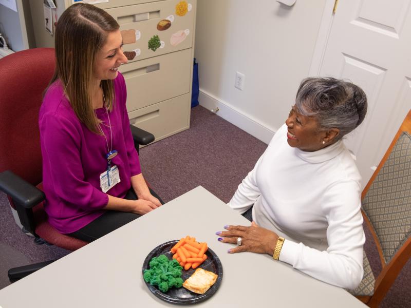 nutrition counselor sitting at a table with an older female patient with a plate of healthy food