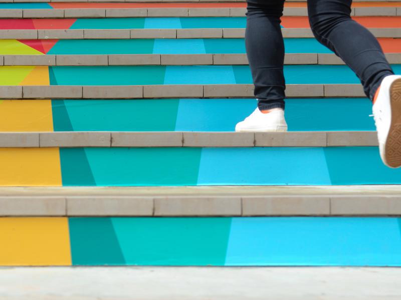 Someone wearing white sneakers walking up a colorful staircase