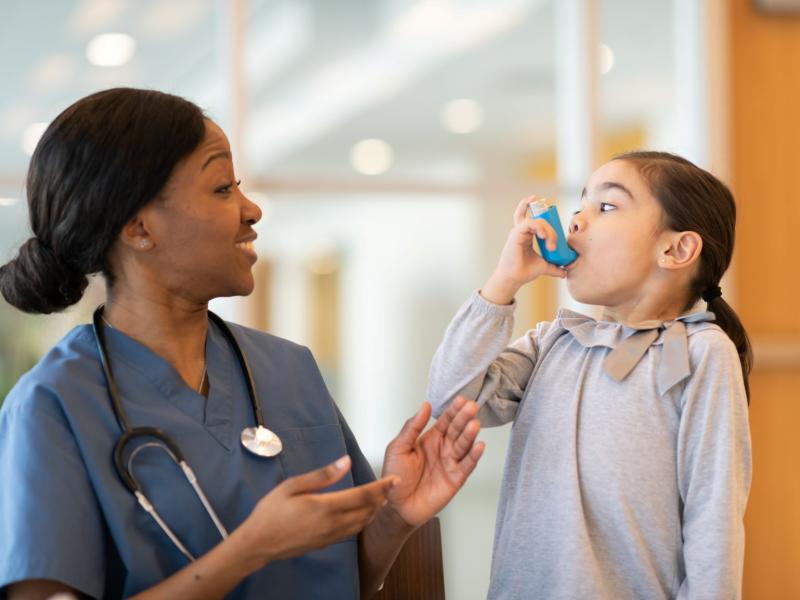 Smiling nurse cheering on little girl using an inhaler