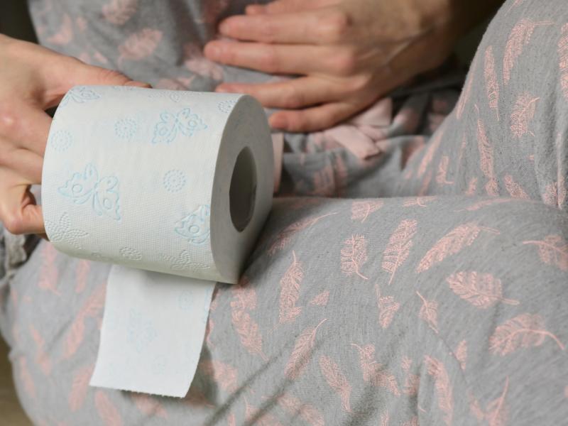 A person holding their stomach and holding a roll of toilet paper