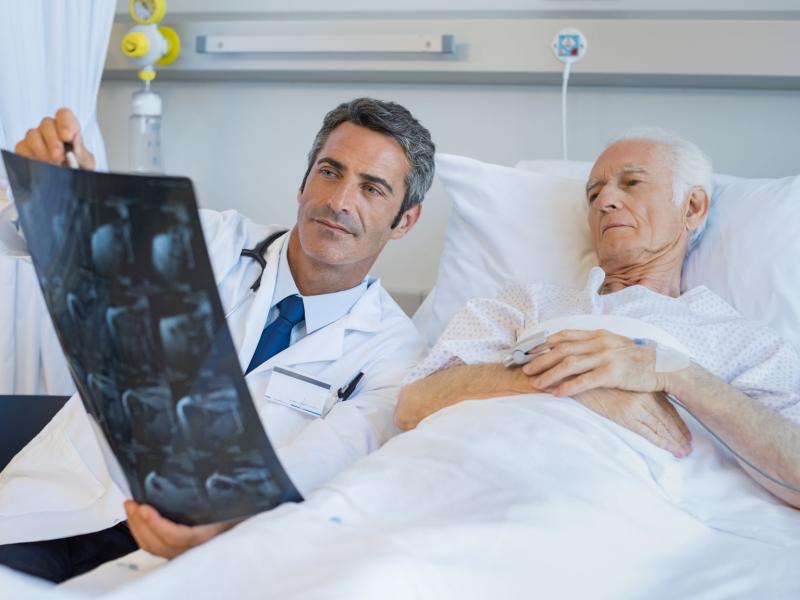 Male physician reviewing x-rays with an older male patient in a hospital bed