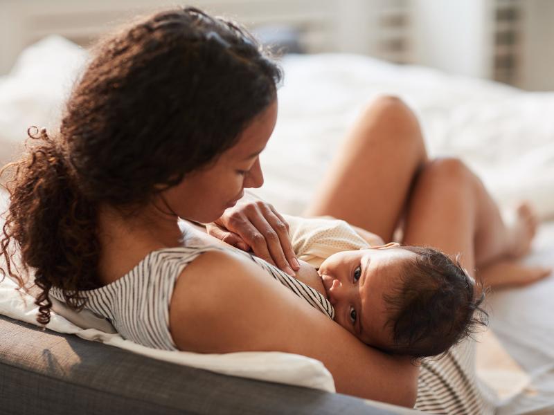 High angle portrait of young African-American mother breastfeeding cute baby boy with child looking at camera, copy space